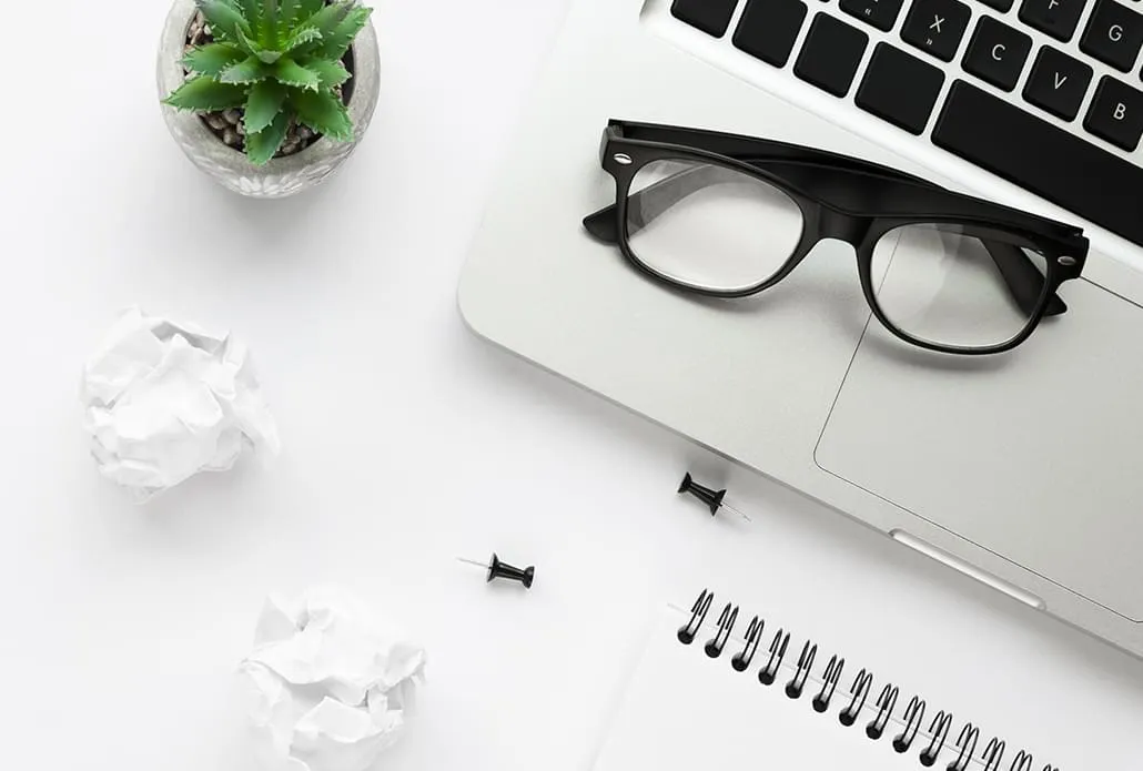 Bureau de travail : ordinateur portable, lunettes, bloc-notes et plante